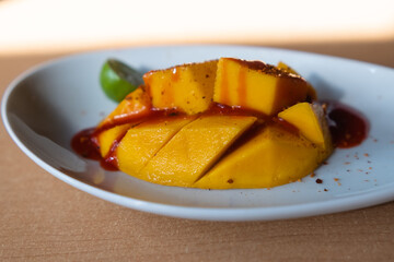 Plate of chopped mango with Mexican chamoy sauce and blurry background