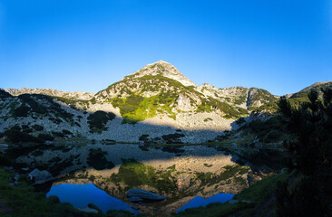 Naklejka na ściany i meble Reflection of rocky Muratov peak in the calm water of Muratovo lakes in Pirin mountain National park in Bulgaria