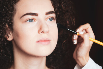 Obraz premium The work of a professional makeup artist. Closeup portrait of beautiful woman getting professional make-up with brush.