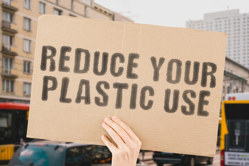 The phrase " Reduce your plastic use " on a banner in men's hand with blurred background. Waste. Customer. Pollution. Earth. Environment
