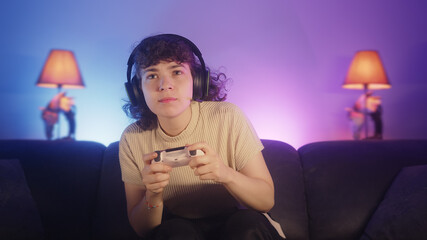 Pretty young gamer woman with headphone sitting on sofa and playing a video games on console with controller © mahirkart