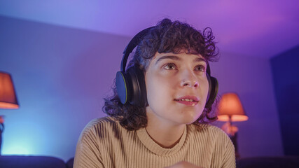 Portrait of beautiful gamer girl with curly-haired. Young girl sitting and playing a video game with headphone