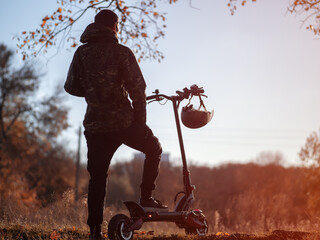 A young man on an electric scooter in autumn at sunset. Modern transport, warm autumn lifestyle