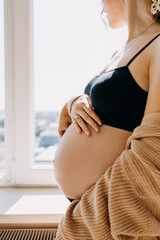 Closeup of a pregnant woman standing by the window in soft light.