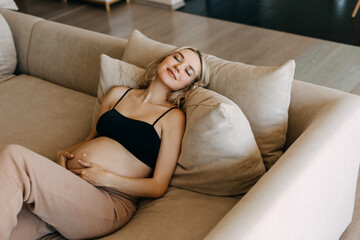 Pregnant woman wearing cozy home wear, lying on a sofa at home, dreaming.