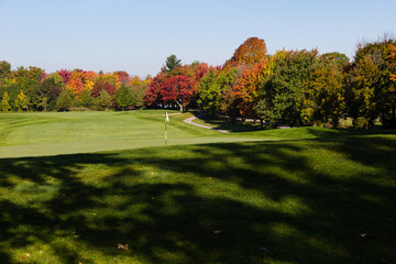 Green flag in golf course with beautiful Fall foliage seen during a sunny morning,...