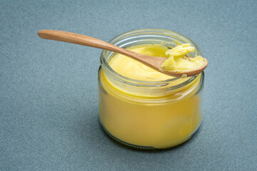 jar and spoon of ghee (clarified butter) on textured paper background
