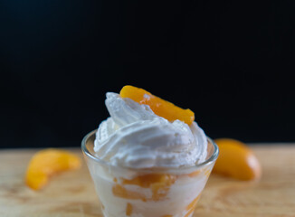 Cup of peaches and cream and fruit slices on wooden surface