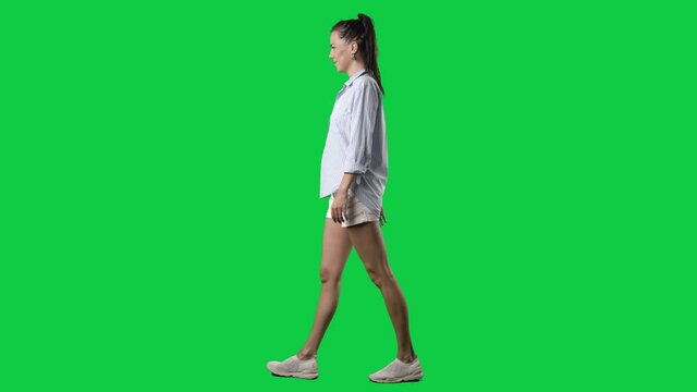 Side view of happy relaxed summer style smart casual woman walking. Full body on green screen chroma key background