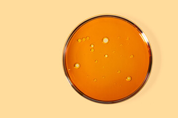 Top view of petri dish with cosmetic oil inside.Yellow background with copy space.