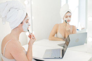 Caucasian woman applying face mask and looking at laptop manual.