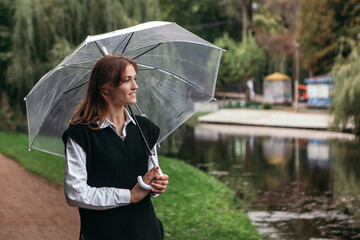 Woman hold transparent umbrella outside wet street autumn near river lake in cloud weather rain...
