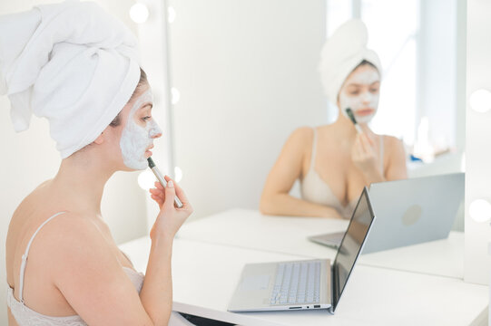 Caucasian woman applying face mask and looking at laptop manual.