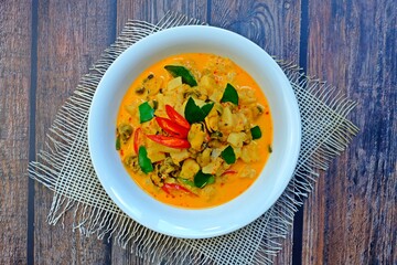 Pineapple red curry with mussels (Gang Kua Subparod) in white bowl on wooden table. Authentic Thai food.