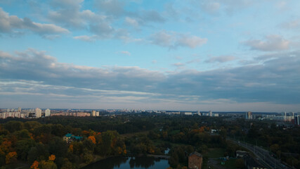 Flight over the autumn park. Trees with yellow autumn leaves are visible. On the horizon there is a blue sky with clouds and city houses. Aerial photography.