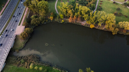 Flight over the autumn park. Trees with yellow autumn leaves are visible. The city highway is visible. The park pond is visible. Aerial photography.
