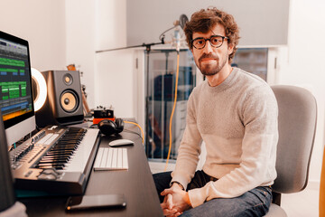 Male music producer working with his computer at home music studio. Millennial musician looking at...