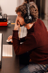Male music producer wearing headphones working with his computer at home music studio