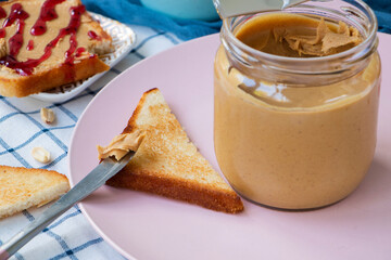 knife with creamy peanut butter on a slice of toast. A full jar of peanut butter and toaster bread on a plate close . Healthy breakfast concept. High quality photo
