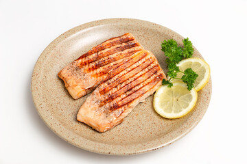 Grilled salmon fillet and lemon slices on a plate. White background. Healthy food. Isolate.