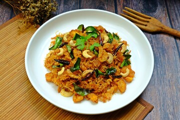 Thai sweet and sour crispy noodles (Mee Krob), crispy rice noodles in white plate on wooden table. Authentic Thai food.