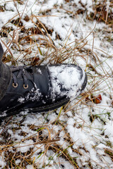 Snow-covered black boot of a man on his feet while walking in a winter park, top view. Man in black boots in the snow