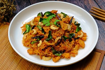 Thai sweet and sour crispy noodles (Mee Krob), crispy rice noodles in white plate on wooden table. Authentic Thai food.