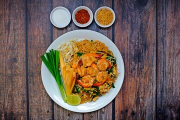 Fried rice noodle with shrimp (Pad Thai Goong Sod) in white plate with sugar, peanut and chili plate on wooden table.