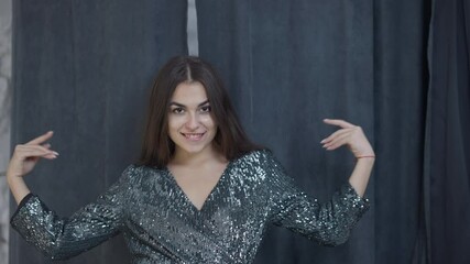 Front view satisfied woman opening curtains in dressing room looking at camera smiling boasting new sparkling dress. Portrait of happy Caucasian shopper posing in elegant apparel indoors in shop