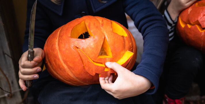 Little girls make jack-o-lantern from big pumpkins for celebratiion of halloween holiday.Witch costume, hat, coat. Cut with knife,take out pulp with seeds.Outdoors activity, backyard.Children's party