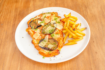 Argentinian veal schnitzel with mozzarella cheese, sliced parmesan cheese, pesto sauce, aubergines, tomato slices and a garnish of homemade chips