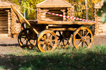 Fototapeta na wymiar An old wooden cart in the park fenced with a special red and white ribbon. Closed public park during quarantine