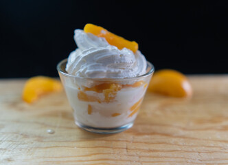 Cup of peaches and cream and fruit slices on wooden surface