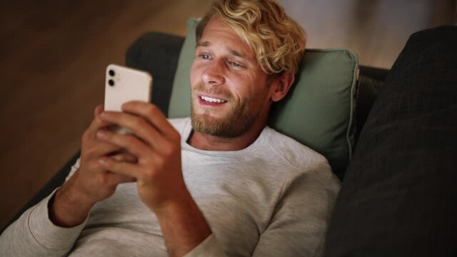 Close-up view of laughing man peering at the phone on the couch