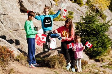 Happy Canada Day. Family of mother with three kids hold large Canadian flag celebration in mountains.