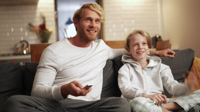 Smiling father and son watching tv and talking on the couch