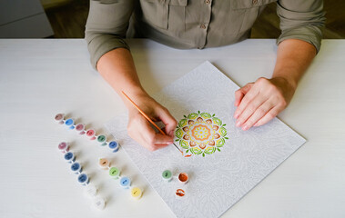 A woman draws a mandala on a white wooden table. Positive thinking and meditation concept. Top view.