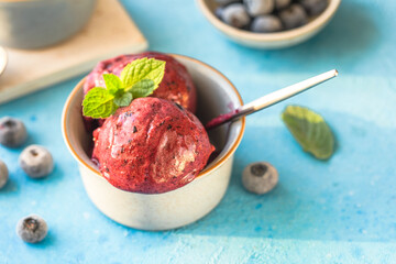 Homemade vegan banana ice cream or gelato with blueberry in a bowl  on blue  background. Healthy dessert.
