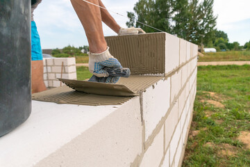Builder uses a notched trowel to apply the cement mixture to the aerated concrete blocks. Concept of building a private house