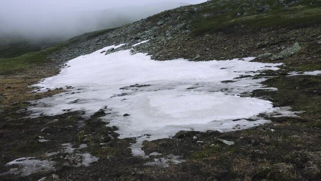 Subniveal belt, altitudinal vegetation zones. Snowfields in the mountains in summer, snow patch on a leeward slope. Low cold clouds creep along the slopes (2700 a.s.l.)