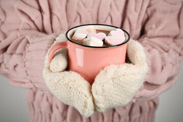 Woman in knitted mittens holding cup of delicious hot chocolate with marshmallows, closeup