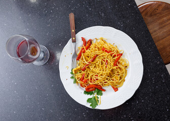 View from above.Marble table with plate of rice noodles with curry, red bell peppers and parsley, and glass of red wine. Vegan food. Enjoying healthy food. No people.