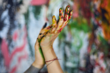 Close up shot of hands in colorful paints of female painter with abstract painting in the background