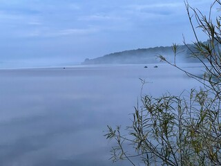 Foggy morning on the lake. Fishermen on boats catch fish in the morning. The sky merges with the lake