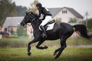 Foto op Canvas portrait of rider man and black stallion horse galloping during eventing cross country competition in autumn © vprotastchik
