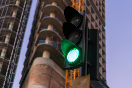 Close-up of a traffic light with an green light signal on the background of a building under construction, yellow crane, sky with copy space