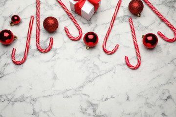 Tasty candy canes, Christmas balls and gift box on white marble table, flat lay. Space for text