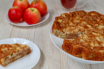 Apple pie on a plate on a wooden table against a background of red apples.