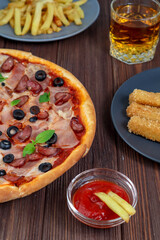 Pizza on a platter close-up on the table with ketchup, juice, sauce and potatoes on a dark wooden table in the rustic style.