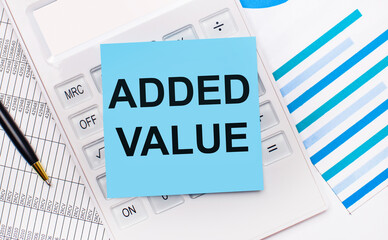 On the desktop is a white calculator with a blue sticker with the text ADDED VALUE, a pen and blue reports. Business concept